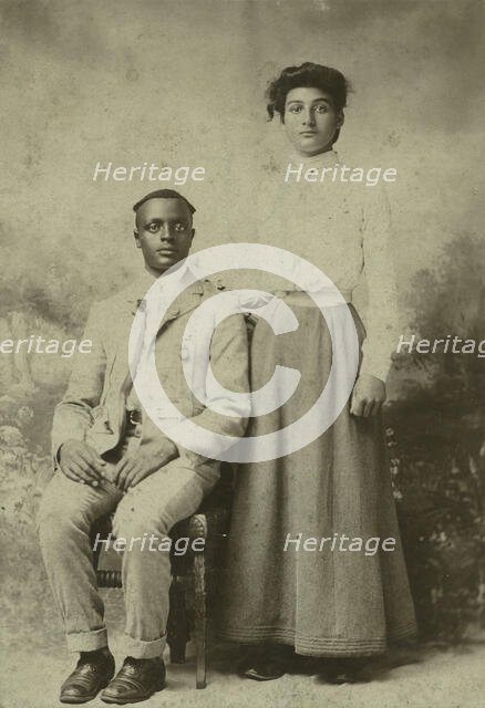 Studio portrait of a young couple, he seated, she with hand on his shoulder, c1900. Creator: Carbon Studio.
