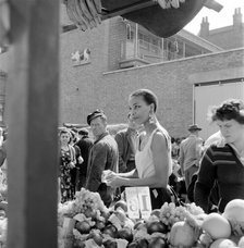 A woman buys fruit at a stall in a North London street market, c1946-c1959. Artist: John Gay
