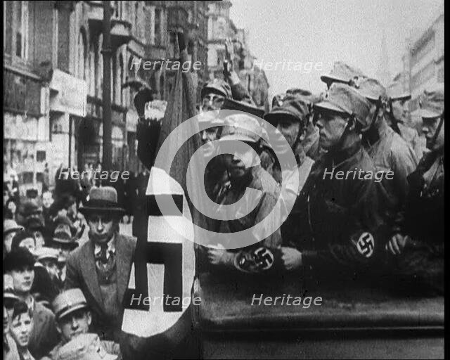 German Civilians and Men in Nazi Uniforms With a Nazi Flag, 1933. Creator: British Pathe Ltd.