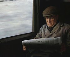 A Man in a Flat Cap and Spectacles Reading a Folded Newspaper in the Window Seat of a Train..., 1938 Creator: British Pathe Ltd.