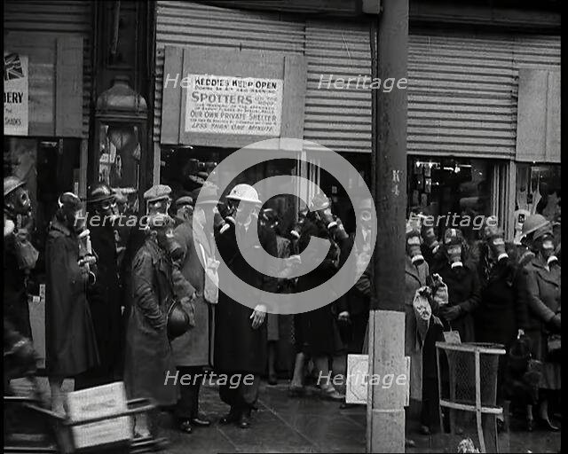 Men and Women Waiting on a Pavement Wearing Gas Masks, 1939. Creator: British Pathe Ltd.