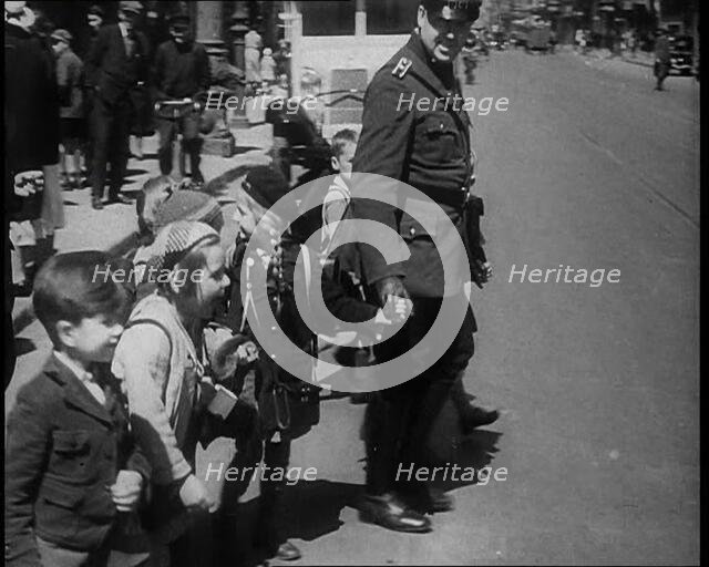 Man in Uniform Helping Young Children Cross the Road, 1933. Creator: British Pathe Ltd.