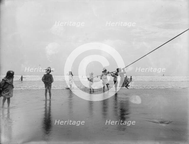 Children swinging on pier rope at beach, between 1900 and 1910. Creator: Unknown.