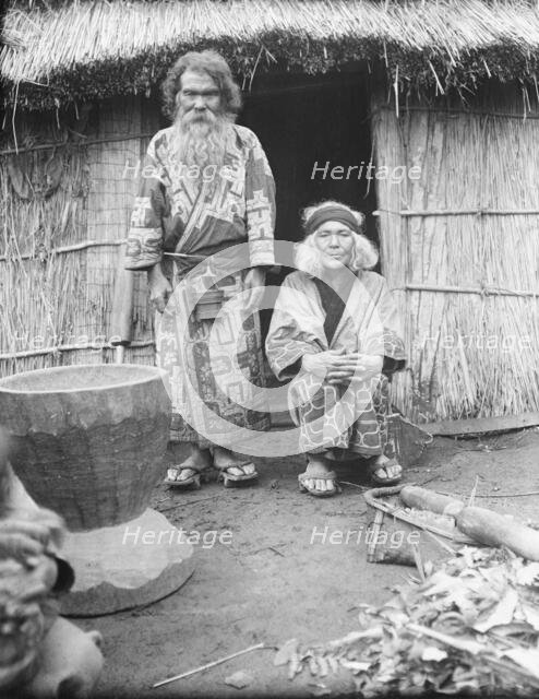 Ainu man and seated woman at the entrance of a hut, 1908. Creator: Arnold Genthe.