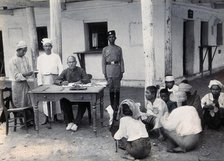 A man sitting at a table examining passports, during a plague epidemic in Mandalay, 1906. Creator: Unknown.