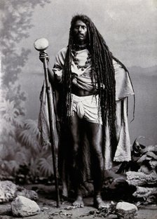An Indian man with long hair, carrying a staff, in a studio setting, 1900. Creator: Unknown.