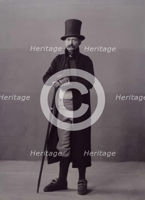 A man poses in folk costume with a long coat and a top hat, 1880-1907. Creator: Helene Edlund.