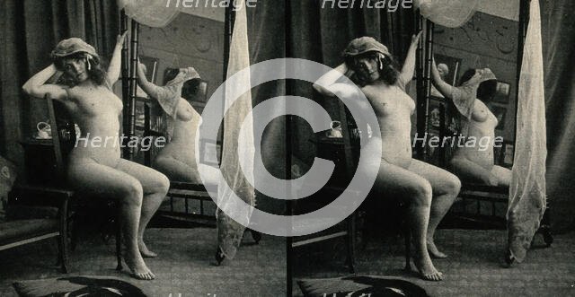 A woman posing naked in a photographic studio, sitting on a chair in front of a looking-glass, c1900 Creator: Unknown.