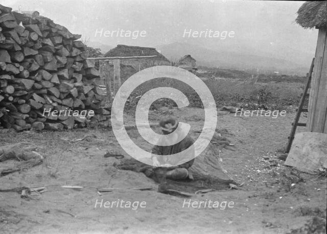 Ainu man seated outside working on nets, 1908. Creator: Arnold Genthe.