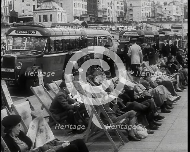 Men and Women Sitting in Deckchairs on the Promenade at  Brighton With a Row of Buses..., 1939. Creator: British Pathe Ltd.