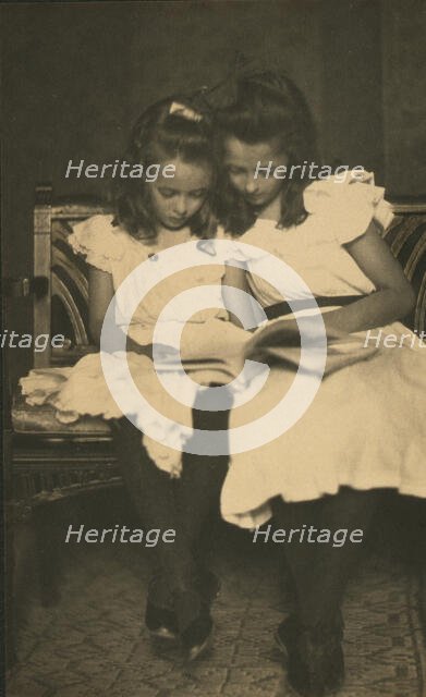 Two girls wearing white dresses and dark stockings reading a book, c1900. Creator: Virginia M Prall.