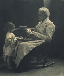 Elderly woman in a rocking chair peeling apple with young girl standing in front of her, c1900. Creator: Elizabeth B. Brownell.