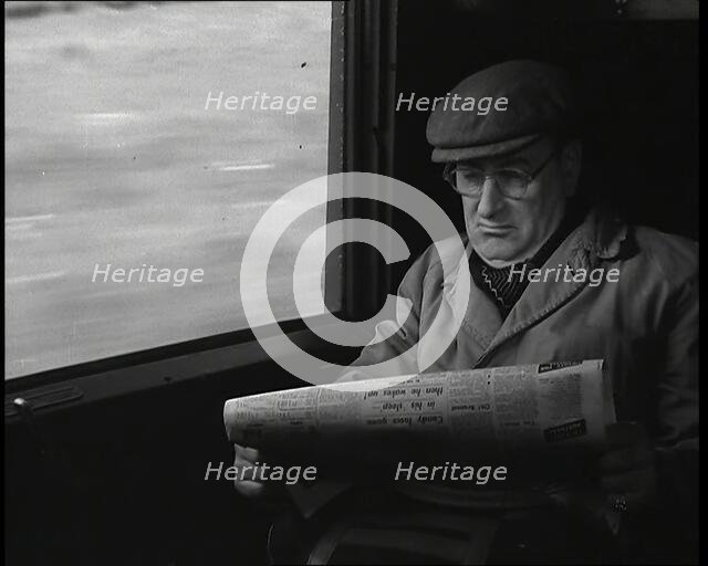 A Man in a Flat Cap and Spectacles Reading a Folded Newspaper in the Window Seat of a Train..., 1938 Creator: British Pathe Ltd.