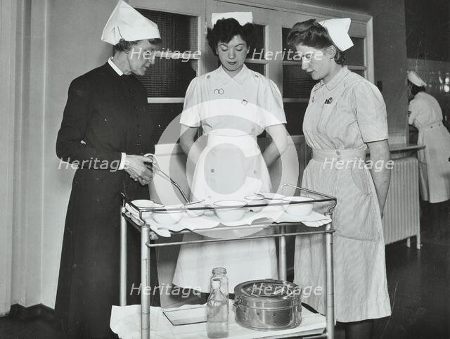 A Sister imparts knowledge and technical expertise to two trainee nurses, c1950s. Creator: Unknown.
