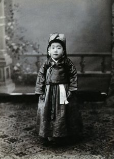 A child posing in front of a painted backdrop in a photographic studio, c1900. Creator: Unknown.