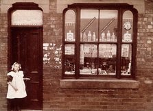A grocer's shop in England: doorway and shop window, (1900?). Creator: Unknown.