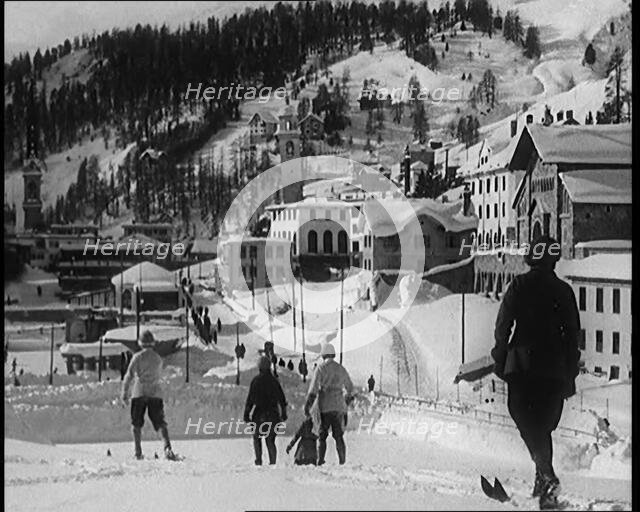 A Group of Female Civilians Skiing down a Snowy Hill with a Picturesque Alpine Village..., 1920. Creator: British Pathe Ltd.