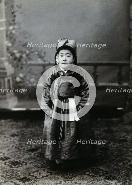 A child posing in front of a painted backdrop in a photographic studio, c1900. Creator: Unknown.