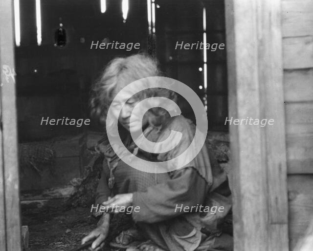 Ainu woman seated in the doorway of a wooden hut, 1908. Creator: Arnold Genthe.