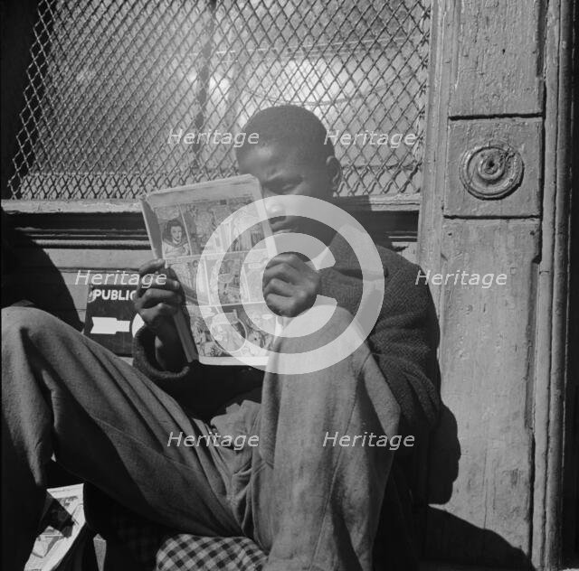 Negro youth reading a funny paper on a door step in the Southwest section, Washington, D.C., 1942. Creator: Gordon Parks.