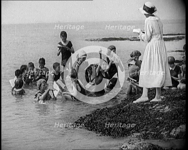 Children Having Swimming Lessons in the Sea While the Teacher Stands on a Rock, 1921. Creator: British Pathe Ltd.