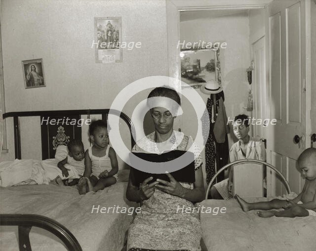Mrs. Ella Watson, a government charwoman, reading the Bible to her household, Washington, DC, 1942. Creator: Gordon Parks.