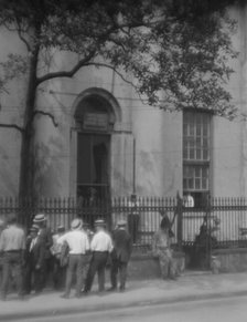 Men standing or sitting in front of the former Bank of Louisiana, 334 Royal Street..., c1920-1926. Creator: Arnold Genthe.
