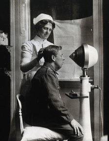 A young uniformed man sitting with a pillow on his chair, facing a machine..., c1910s. Creator: Unknown.