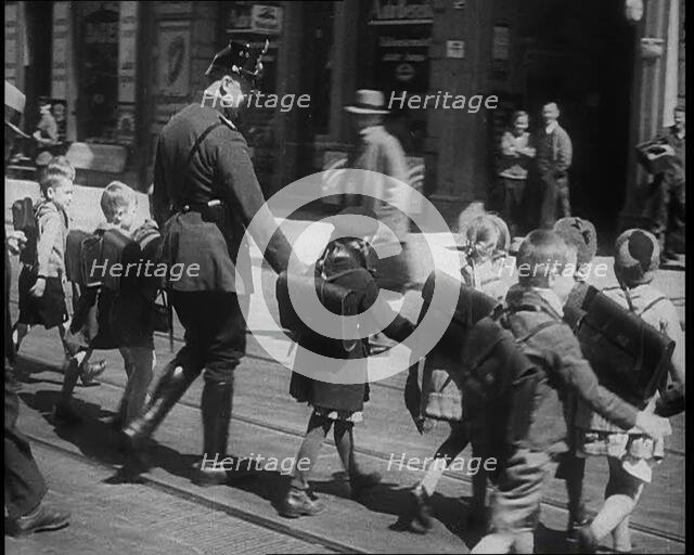 Man in Uniform Helping Young Children Cross the Road, 1933. Creator: British Pathe Ltd.