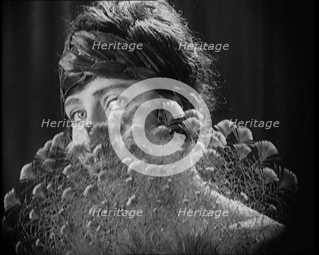 Female Civilian Wearing a Headband Hiding Her Face Behind a Feathers Fan, 1920. Creator: British Pathe Ltd.