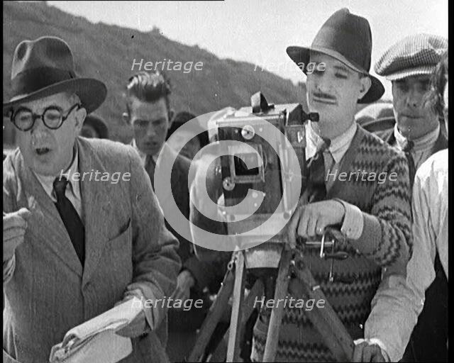A Male Cameraman Cranking a Camera On a Film Set as the Male Director Instructs Actors, 1920s. Creator: British Pathe Ltd.