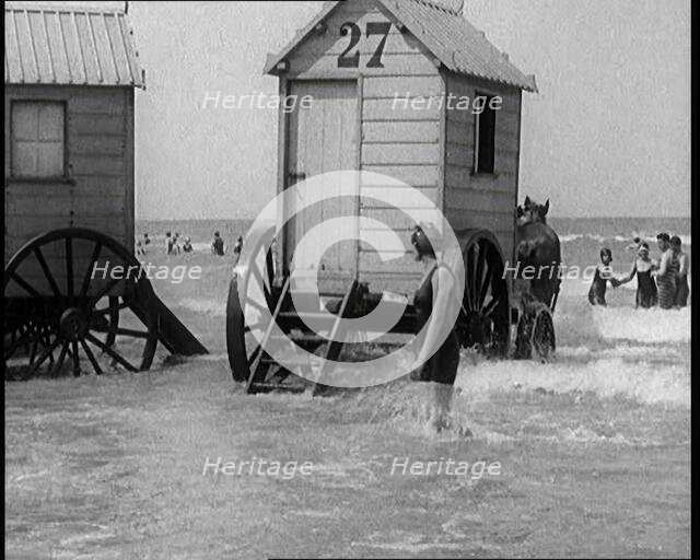 Female Civilian in Bathing Suit Standing in the Sea Watching Changing Cabins on Wheels Being...,1924 Creator: British Pathe Ltd.
