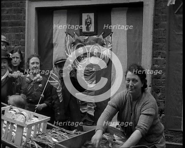 Woman and Others Standing Behind a Street Stall With Wall Behind Decorated With Flags..., 1937. Creator: British Pathe Ltd.
