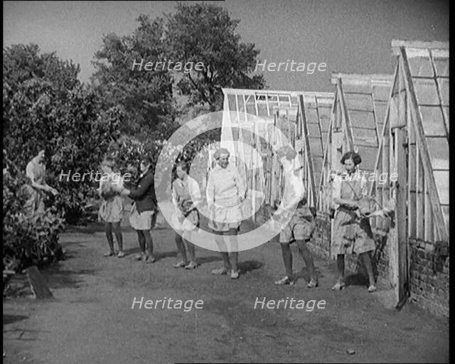 Young Female Civilians Outside a Greenhouse Standing in a Row Passing Plant Pots Along..., 1920. Creator: British Pathe Ltd.