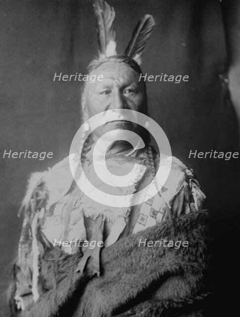 Yellow Horse-Yanktonai, half-length portrait, standing, facing slightly right, with long..., c1908. Creator: Edward Sheriff Curtis.