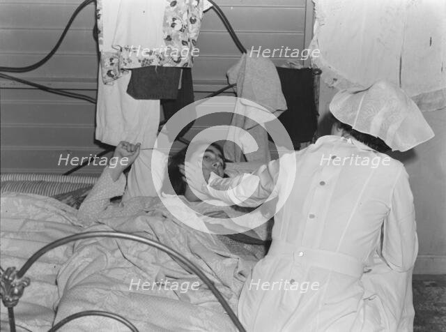 Nurse attending sick migrant woman, FSA camp, Farmersville, Tulare County, California, 1939. Creator: Dorothea Lange.