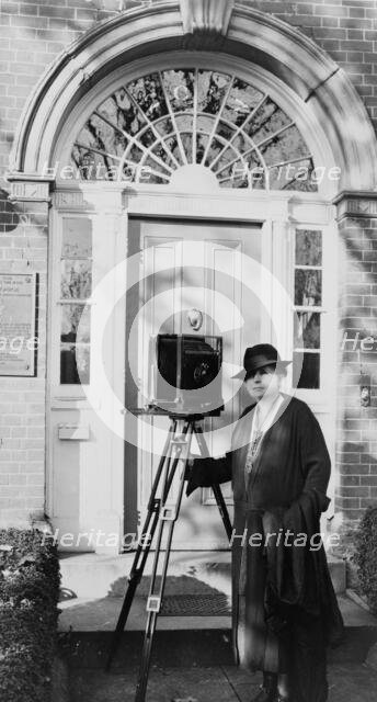 Frances Benjamin Johnston, full-length portrait, standing in front of door, with camera..., c1935. Creator: Unknown.