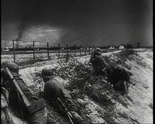 Four Male German Army Soldiers Lying Low on a Slope Below a Fence While Columns of Smoke..., 1939. Creator: British Pathe Ltd.