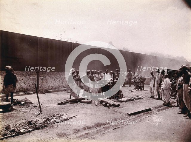 A group of men stand around the body of a man laid out on a pyre of logs during a Hindu...,  1896/97 Creator: Unknown.