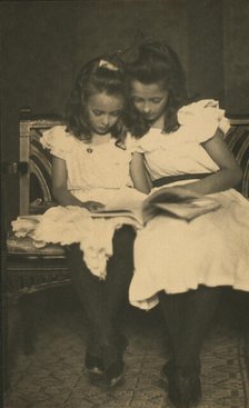 Two girls wearing white dresses and dark stockings reading a book, c1900. Creator: Virginia M Prall.