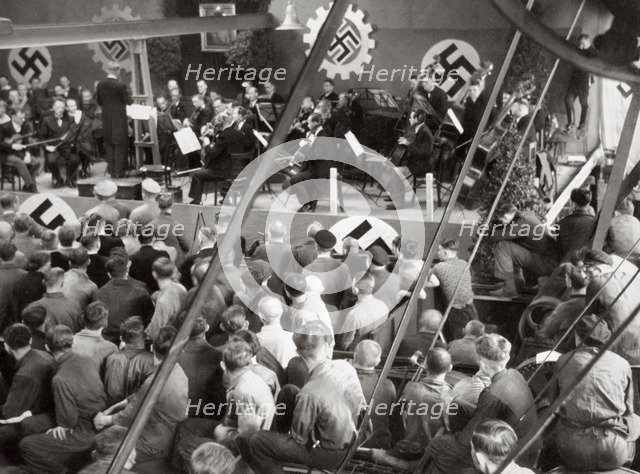 An orchestra plays to some factory workers as they take a break from work, Germany, 1936. Artist: Unknown