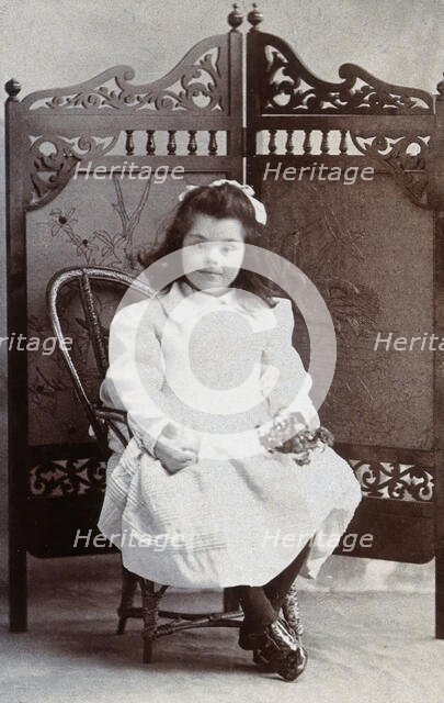 A girl with Down's syndrome, sitting in front of an ornate wooden screen..., c1870s. Creator: Charles Marshall.