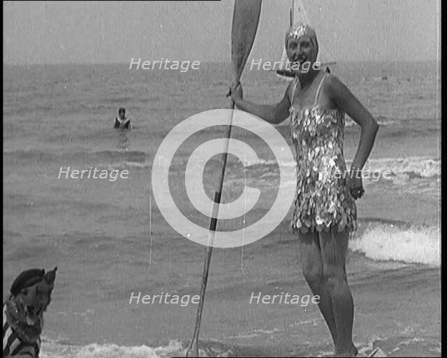 Female Civilian Wearing a Sequinned Swimsuit with a Dog in a Striped Shirt and Beret on a Canoe,1920 Creator: British Pathe Ltd.