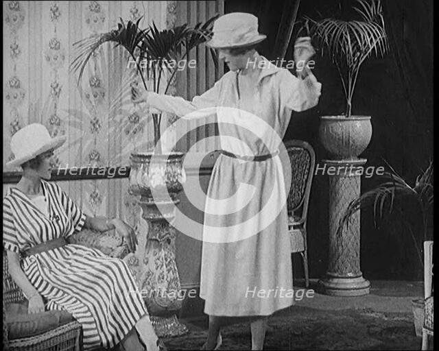 Two Female Civilians Leisuring in a Drawing Room Wearing Long Dresses and Hats Comparing..., 1920. Creator: British Pathe Ltd.