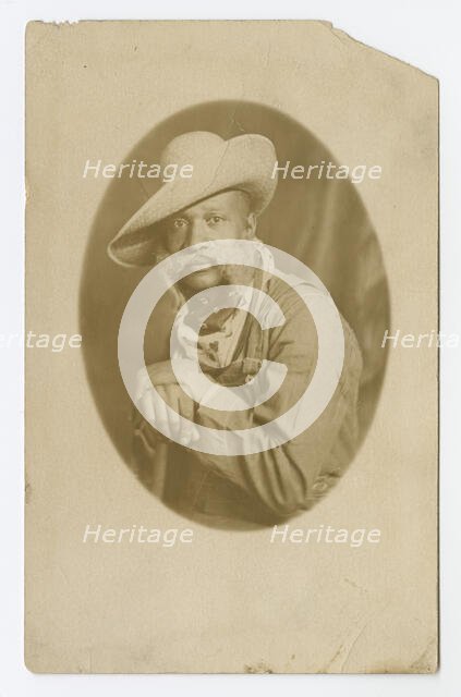 Photographic postcard portrait of a man wearing a hat and overalls, early 20th century. Creator: Unknown.