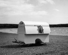 Woman smiling from the window of a trailer caravan on a beach, (c1960s?). Artist: Unknown