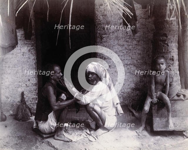 Two Indian men crouching; one is cutting the other's hair, while a girl sits.., c1890s.  Creator: Unknown.