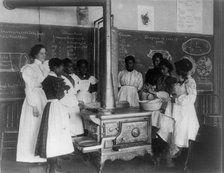 African American schoolgirls with teacher, learning to cook on a wood stove in classroom, (1899?). Creator: Frances Benjamin Johnston.