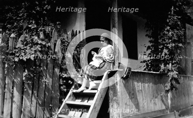Woman sewing on her porch steps, Bistrita Valley, Moldavia, north-east Romania, c1920-c1945. Artist: Adolph Chevalier