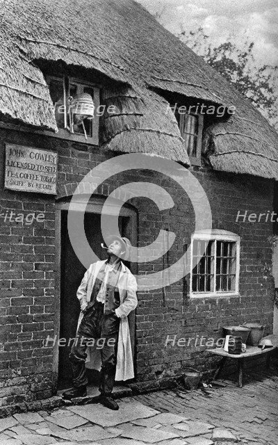 A man smoking a pipe outside a shop, Worcestershire, c1922.Artist: AW Cutler